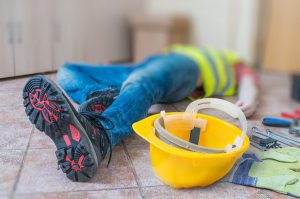 Foto de la pierna y el casco amarillo de un trabajador tendido herido en el trabajo