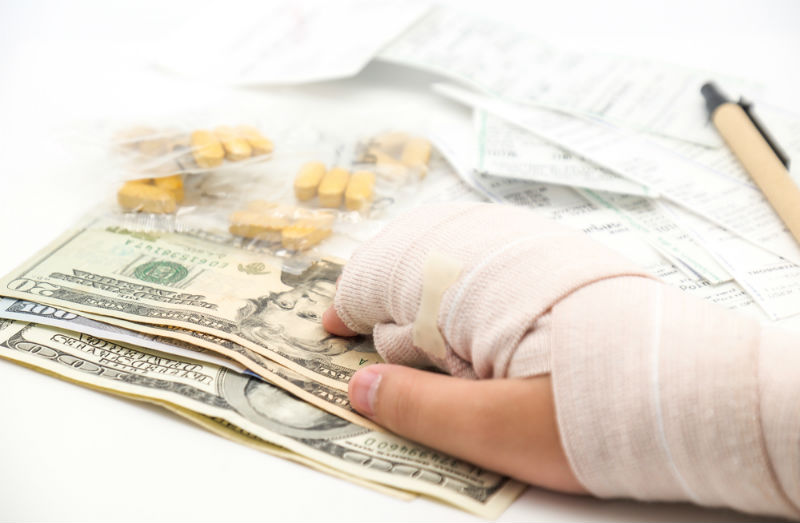 A hand in a cast receiving a stack of money, with painkillers and prescriptions in the background - Riddle & Brantley