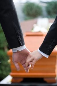 Two people viewing a casket and holding hands