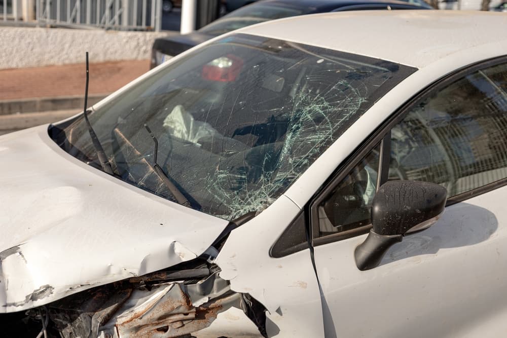 car showing extensive front-end damage after collision, highlighting shattered windshield and deformed hood. 