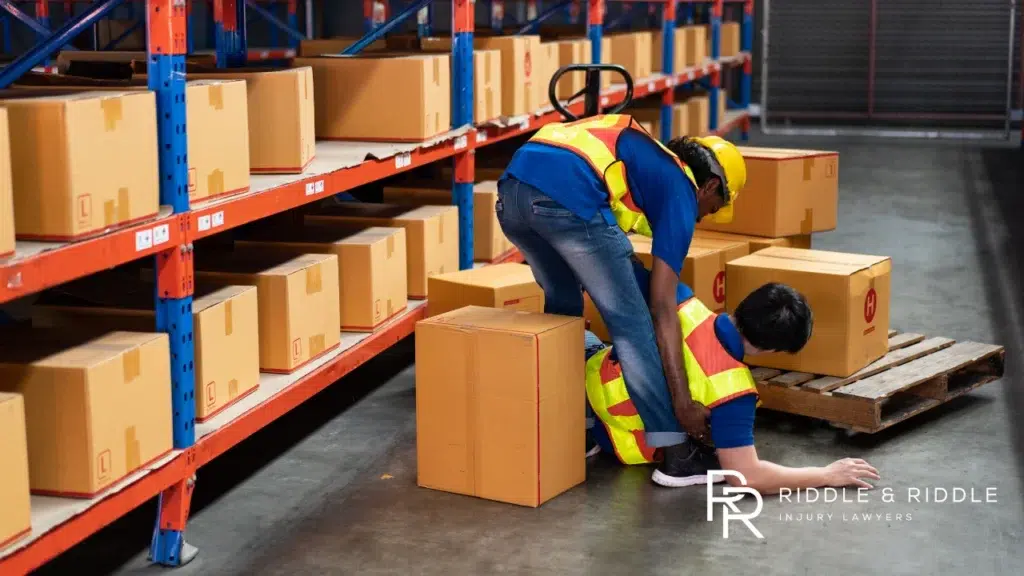 Worker in a safety vest collapses while lifting heavy boxes in a warehouse