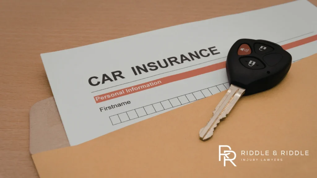 Close-up of a car key sitting on top of a CAR INSURANCE policy document