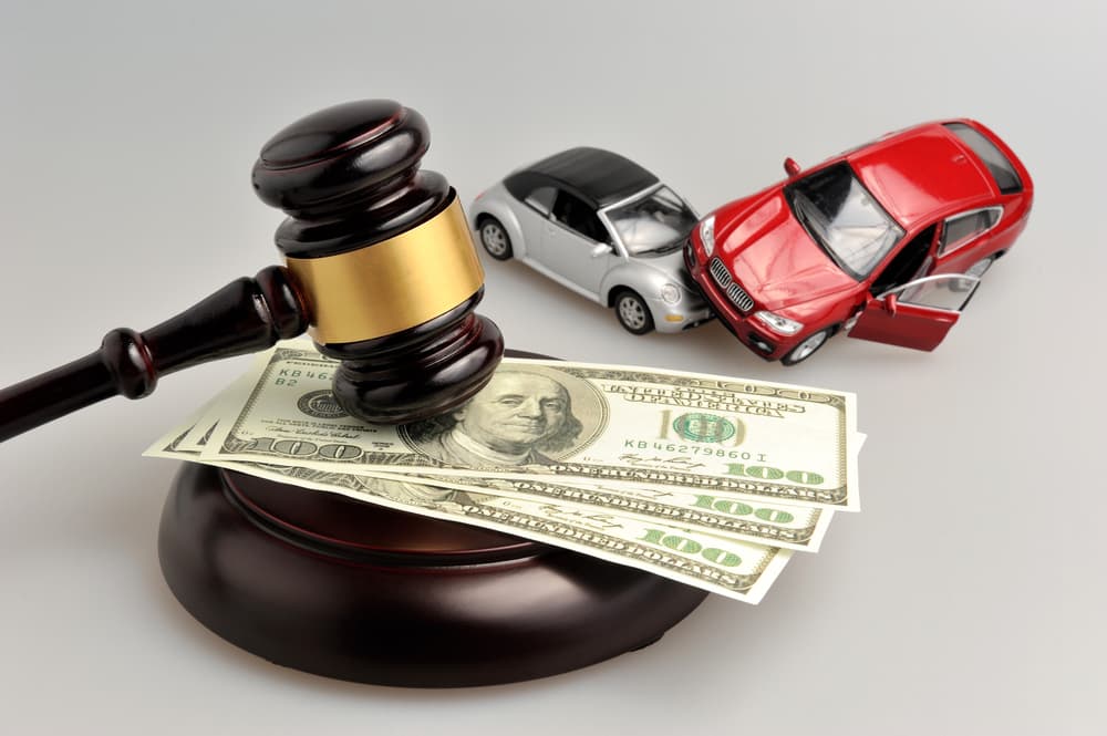A judge's gavel, along with currency and toy cars, displayed against a gray background.