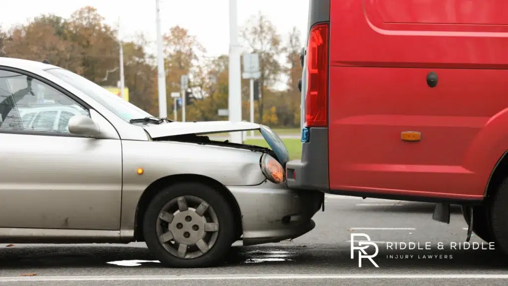 Silver car with a crumpled hood after crashing into the back of a red van