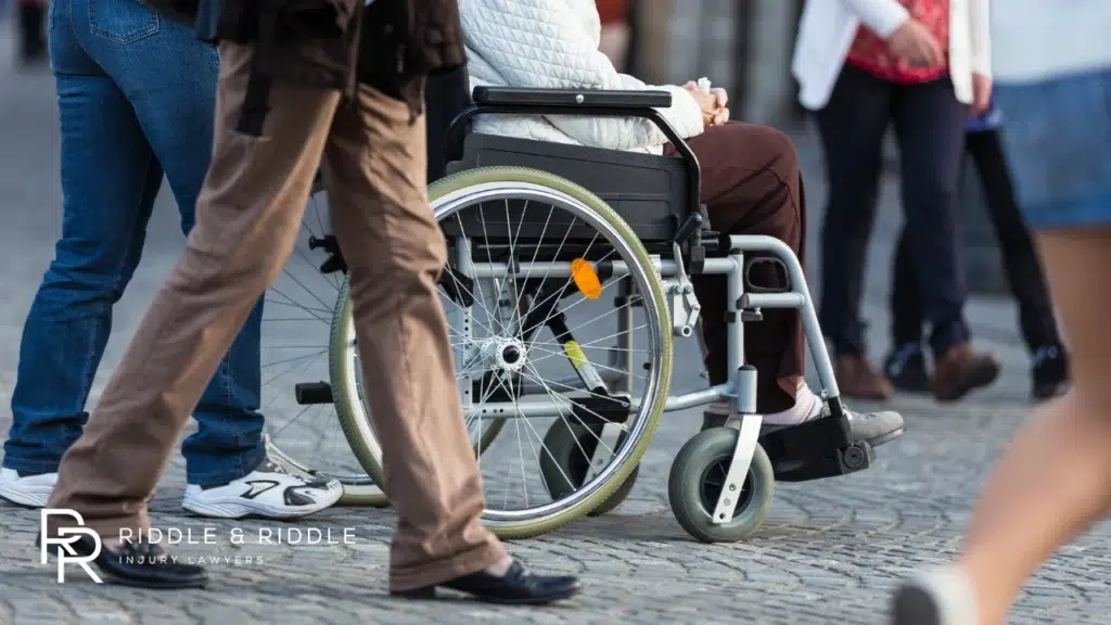 Low-angle shot of people walking on a city sidewalk, including one person in a wheelchair