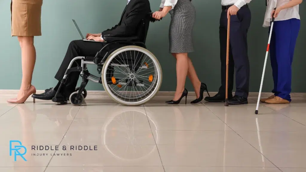 Lower-body view of people standing in line, including a person using a wheelchair and a cane