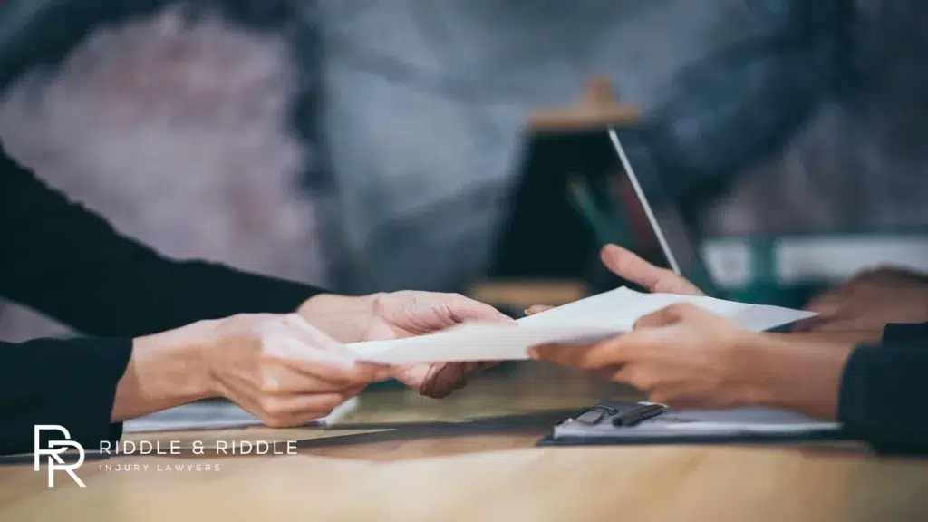 Close-up of hands exchanging and signing legal documents over a wooden desk