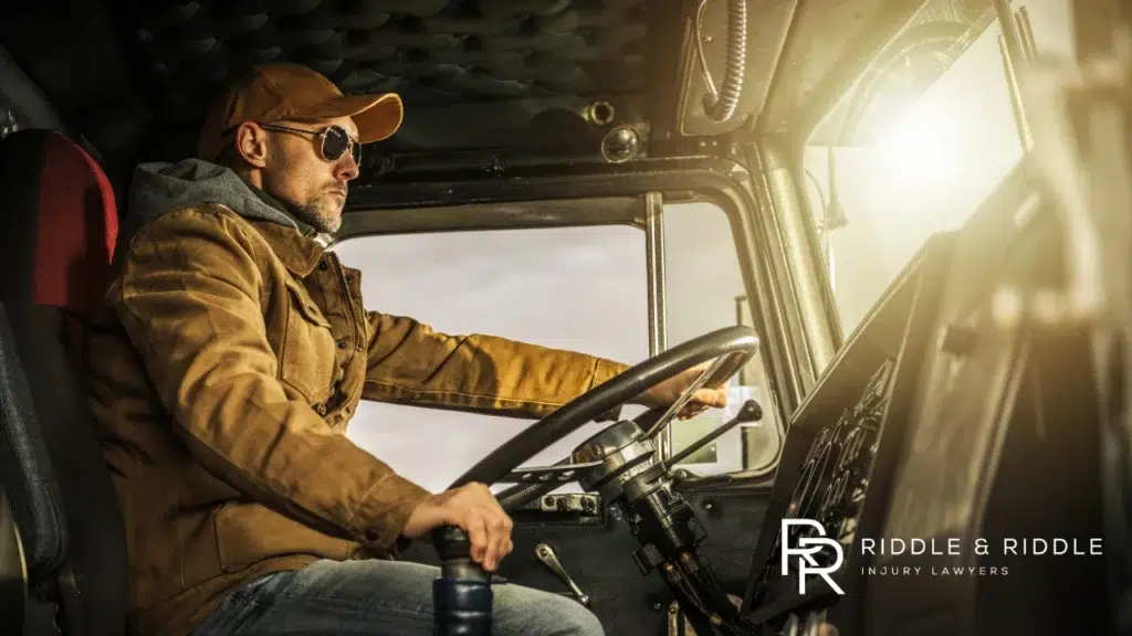 Man in a brown jacket and baseball cap driving a large commercial truck