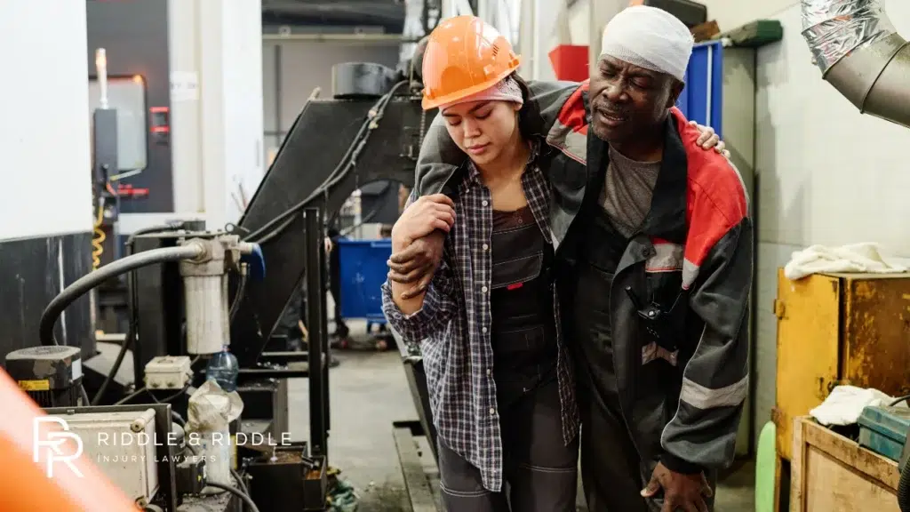 Man in a hard hat helps an injured coworker in an industrial factory setting