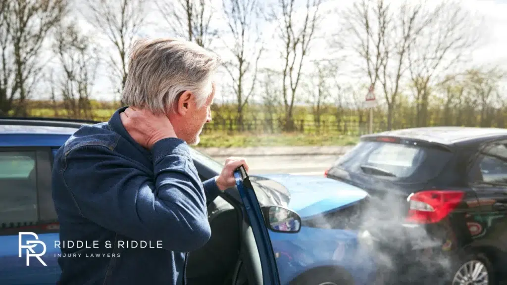Man looks under the hood of a car with smoke billowing out after an accident