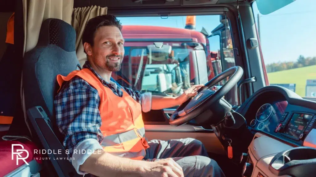 Happy man in a plaid shirt sits in the cab of a semi-truck holding the steering wheel