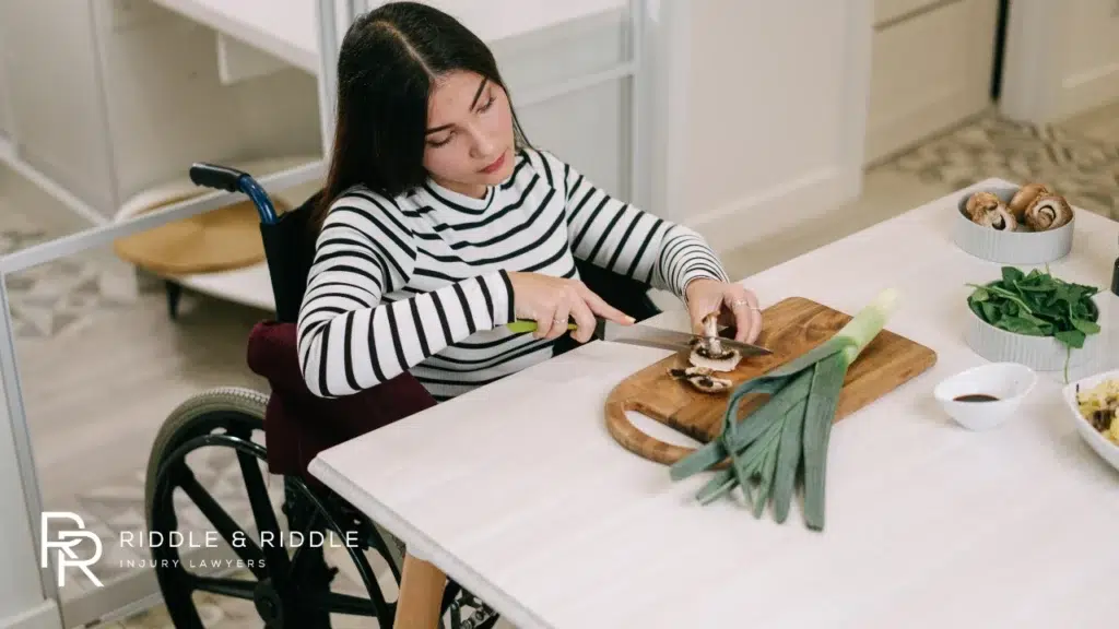 A woman in a wheelchair prepares vegetables at a kitchen table
