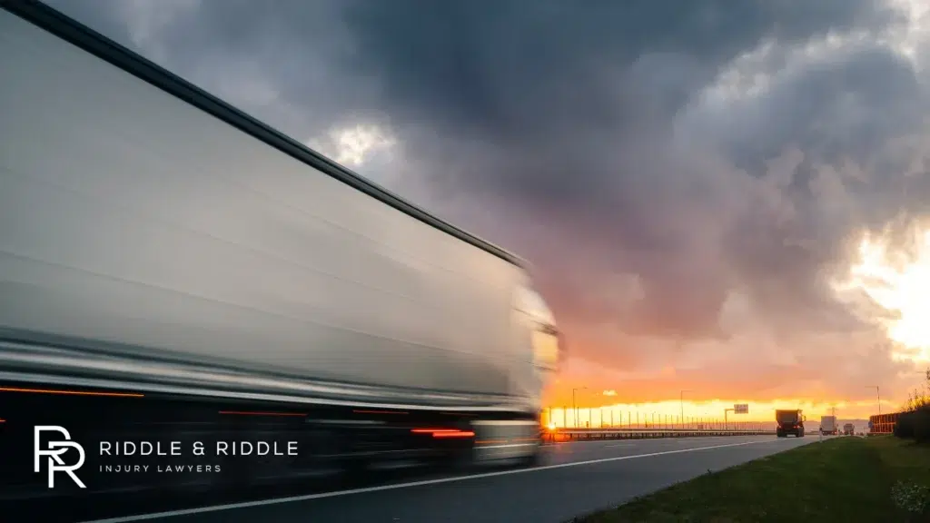 Semi-truck travels down a highway at high speed during a golden sunset