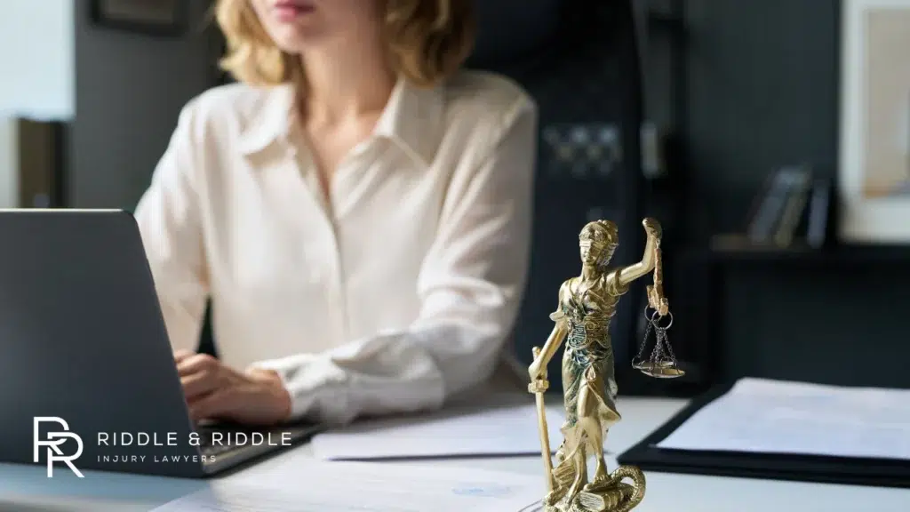 Professional woman sits at a desk featuring a Lady Justice statue and law books