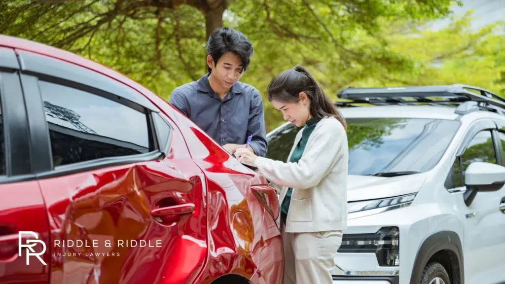 A man and woman examine a dent on the rear of a red car after an accident