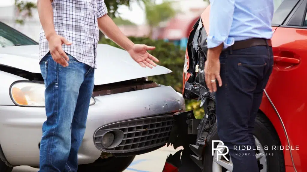 Two men stand between two crashed cars, gesturing at the damage on a street