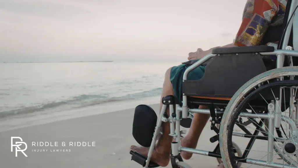 Person sitting in a wheelchair looks out over the ocean at the beach during sunset