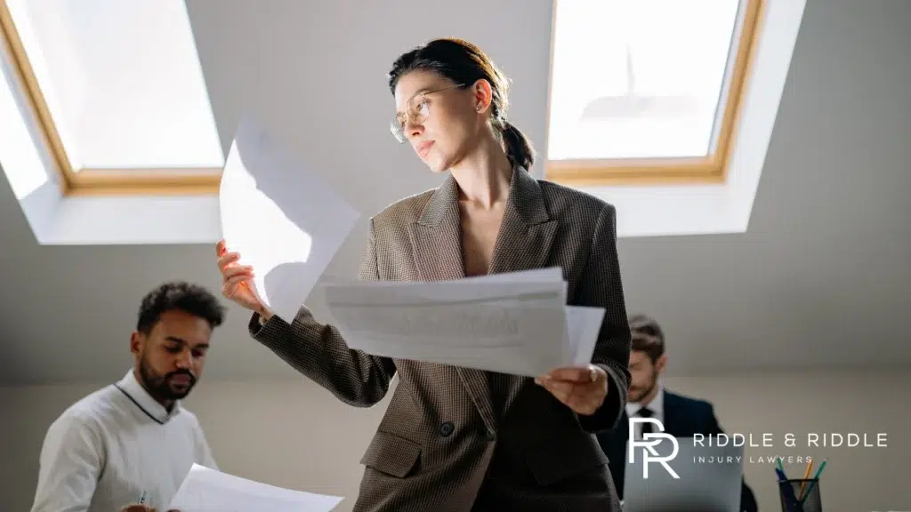 Female lawyer stands while reviewing papers with colleagues at a conference table