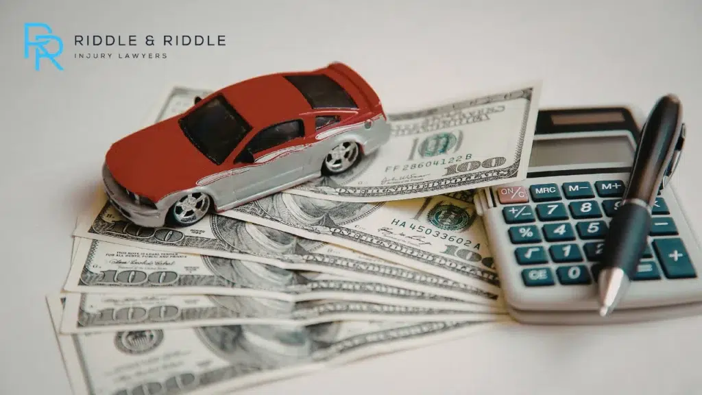 Close-up image of a small car, pen, calculator and hundred dollar bills