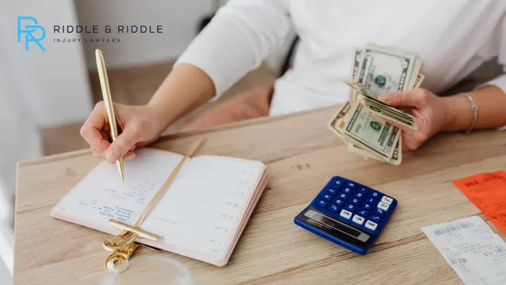 Person holding money in right hand while holding pen in left hand and writing on notebook
