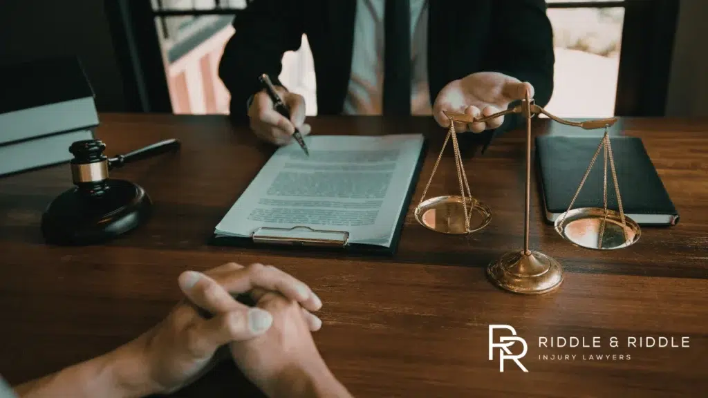 Hands clasped on a desk next to a signed document, a judge’s gavel, and scales of justice