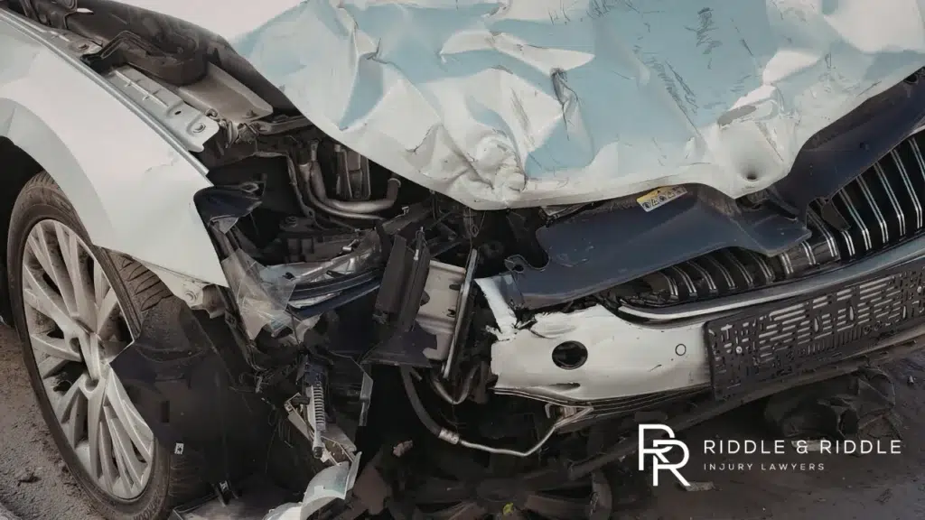 Close-up of a white vehicle with significant front-end damage and a shattered headlight