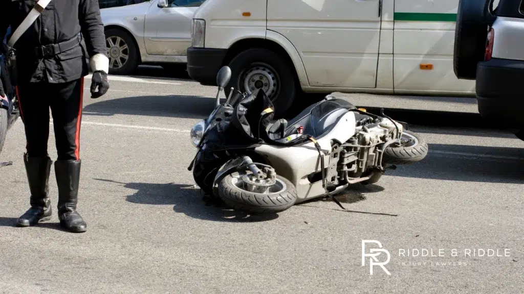 A motorcycle lies on its side on the road next to a white van with an officer nearby