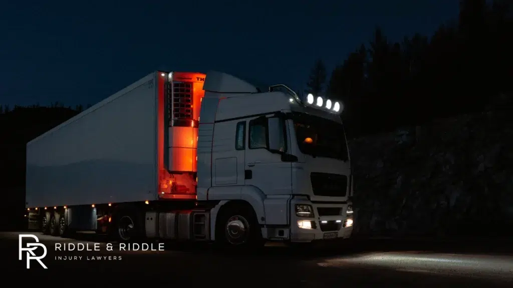 A large white commercial semi-truck parked at night with red lights glowing in the trailer gap