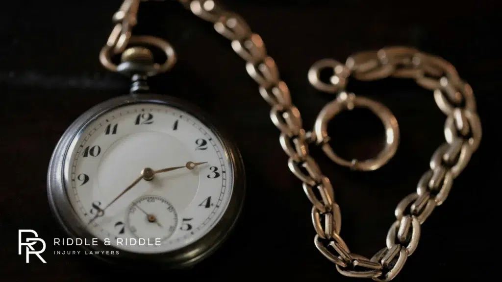 A vintage silver pocket watch with a chain draped over a dark surface
