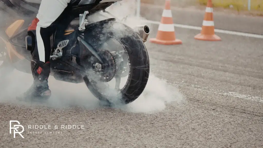 Motorcycle tire creates a cloud of smoke during a heavy skid near orange traffic cones