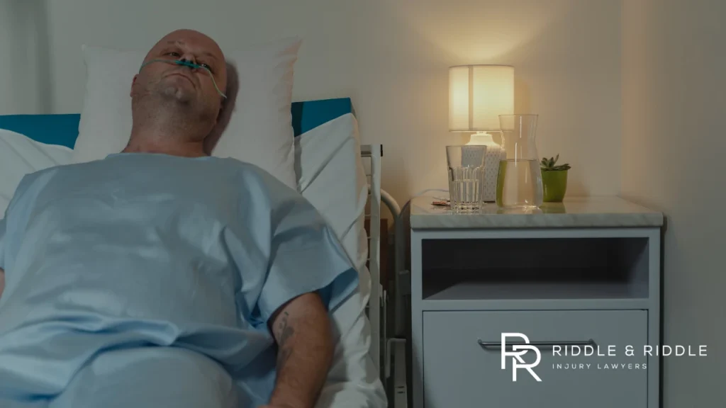 Man lies in a hospital bed wearing a gown and a nasal cannula for oxygen