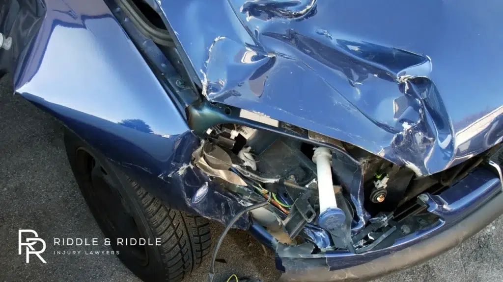 Extreme close-up of a blue vehicle with a shattered headlight and crumpled hood