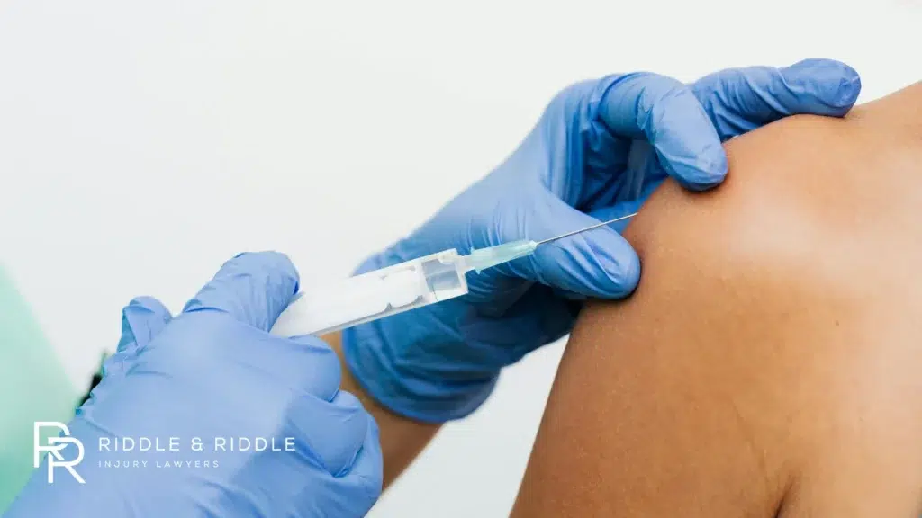 A healthcare worker in blue gloves administers an injection into a patient's shoulder