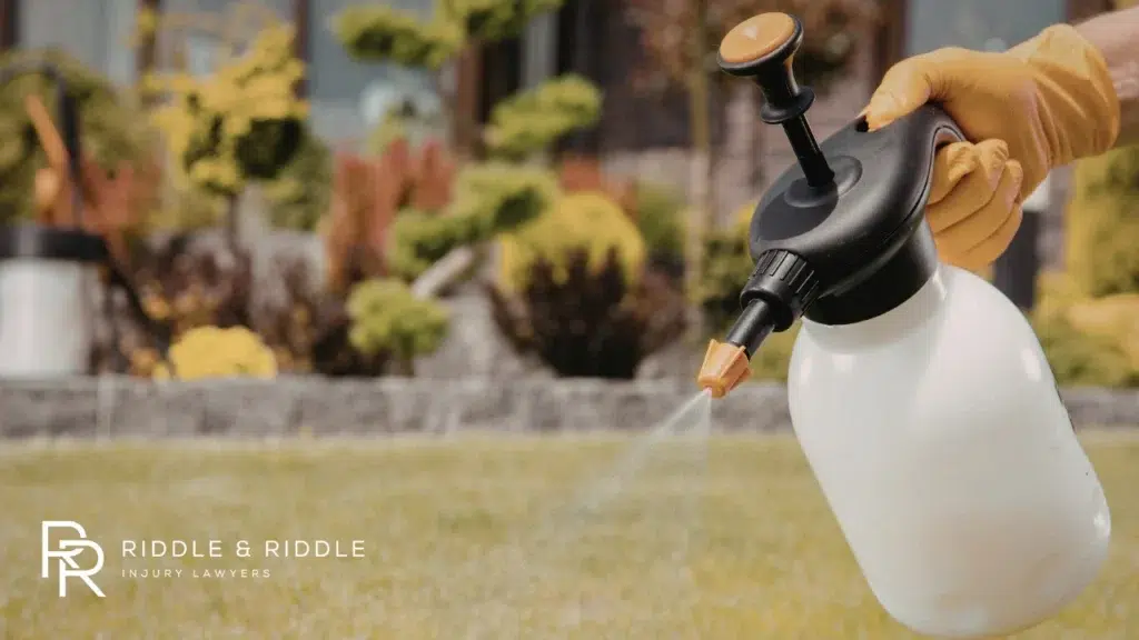 Person in yellow gloves uses a handheld pressure sprayer in a backyard garden