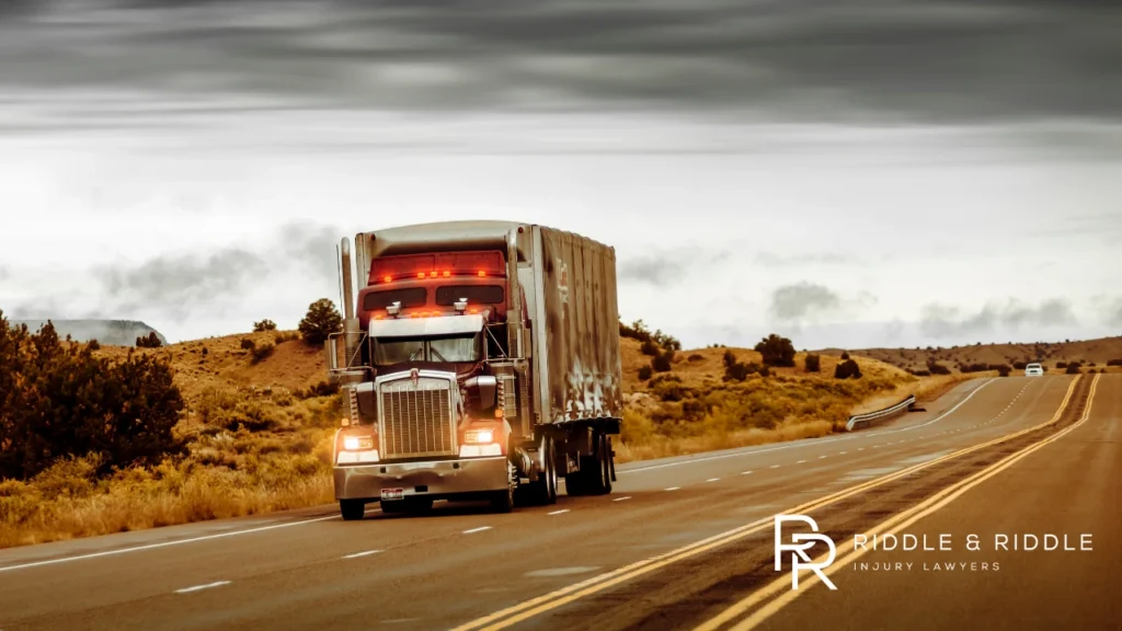 Large semi-truck hauling a trailer drives down a desert highway under a cloudy sky