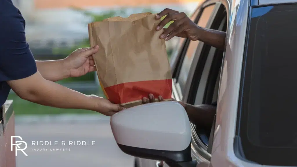 Person in a car receives a brown paper bag from a delivery person at a window