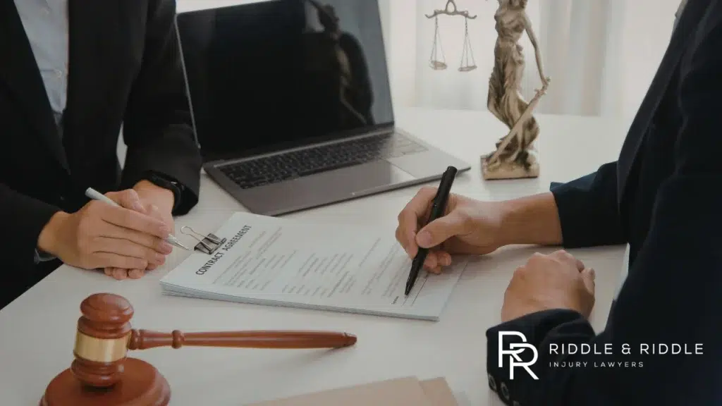 Person signs a document at a desk with a gavel and a Lady Justice statue nearby