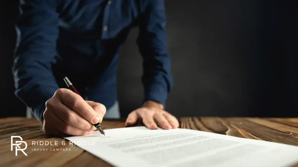 Person in a blue shirt uses a pen to sign a legal document on a desk