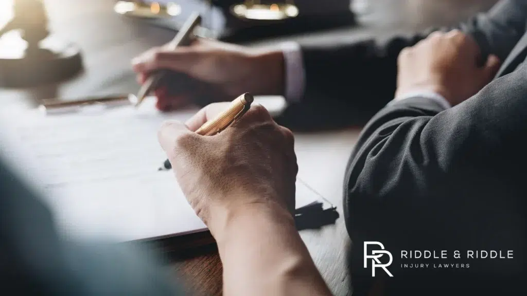 Person's hands hold a pen over documents while meeting with an attorney in a suit