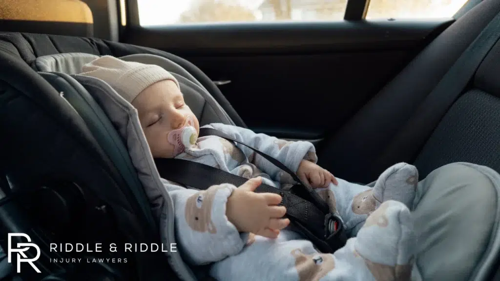 Sleeping baby with a pacifier securely buckled into a gray car seat