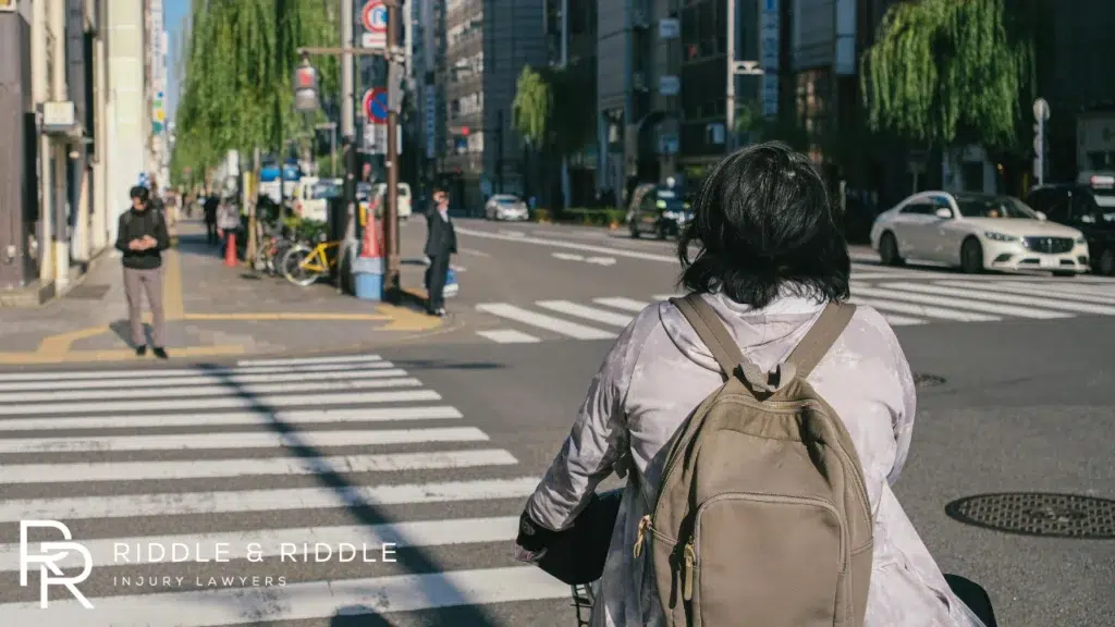 Someone with a backpack at a crosswalk on a sunny city street